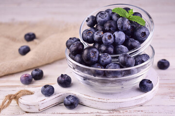 Fresh blueberries in a glass bowl on a white wooden background.
