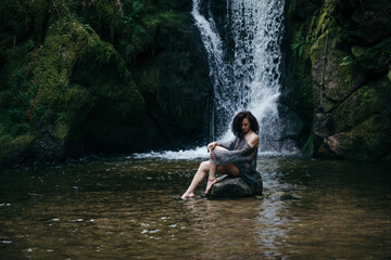 Fototapeta premium Beautiful young woman sitting on rock near mountain river in forest. High quality photo