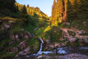 Summer mountain landscape at sunset, a small stream flows into a stormy river on a slope with a...
