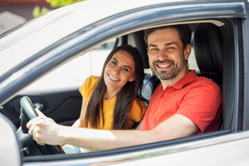 Cheerful millennial couple travellers smiling from car window