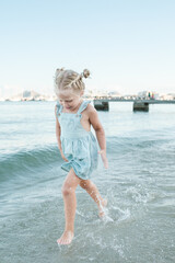 Cheerful little girl in cotton dress playing in wavy sea