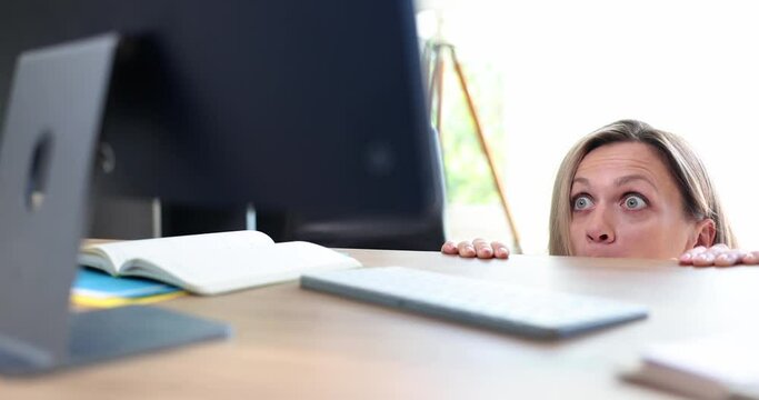 Shocked frightened female secretary peeking out under table and looking at computer screen 4k movie slow motion. Negative news on internet concept