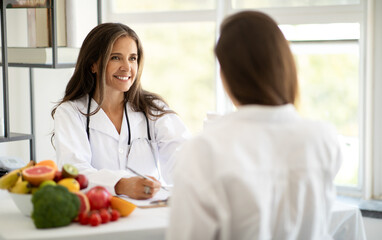 Cheerful european middle aged doctor nutritionist in white coat advises woman patient, recommends...