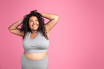 Portrait of happy plump african american woman in sportswear posing over pink background, looking...