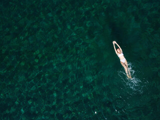 Above view of woman swimming at sea. Aerial top view of young girl in white swimsuit floating on...