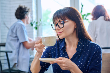 Relaxed middle aged woman enjoying fragrant cup of coffee, in coffee shop