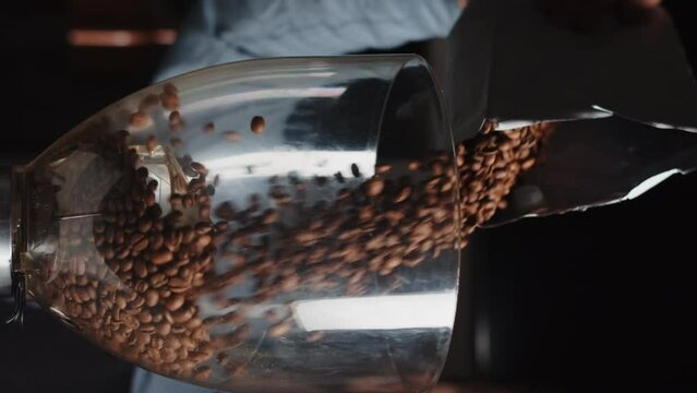 Close up of barista pours coffee beans into a coffee grinder from package in slow motion. Vertical video template for smartphone web promo.