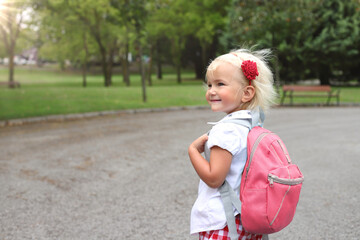 Fototapeta premium Little blond girl with pink rucksack in park, lifetyle going to school
