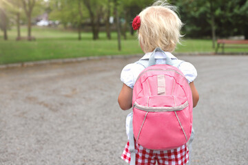Little blond girl with pink rucksack in park, lifetyle going to school