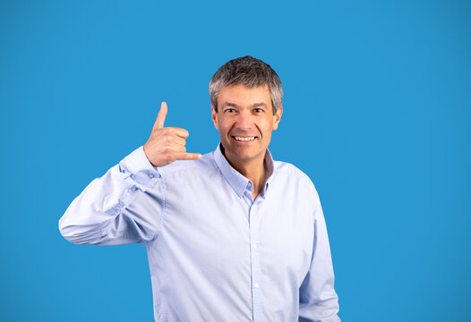 Mature gray man showing call me gesture over blue background