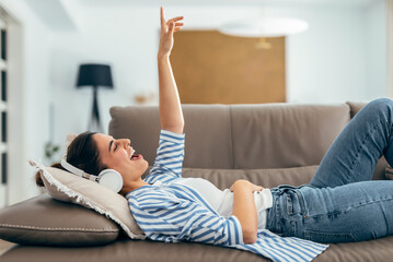 Beautiful woman singing while listening music lying on couch in living room at home