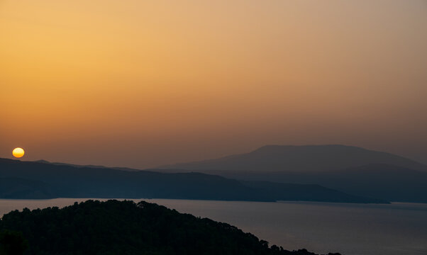 Sunset over the Greek mainland. Picture taken from Skiathos of a warm orange sunset with rolling hills in shades of shadow. 