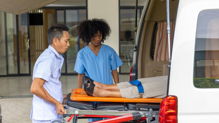 Two paramedic rescuers helping a patient after having an accident. African nurse works with her colleague using stretcher to move a patient to ambulance van. © Ron