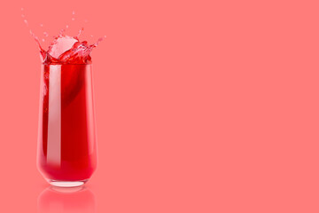 Berry red cold juice in glass with reflection, bright splashes, drops flying, swirl on pastel pink background, copy space. Refreshing healthy summer beverage with splashing.