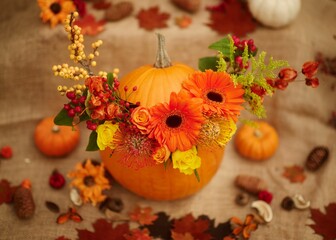 Orange pumpkin with a vibrant floral centerpiece surrounded by autumnal decorations and foliage
