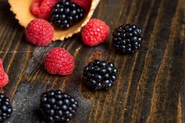 Red ripe raspberries with waffle cups on a black table