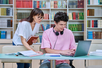 Woman mentor teaching male student in college library, exam preparation