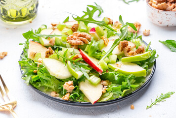 Waldorf salad with apples, green celery, lettuce, arugula and walnuts on plate, white background, top view