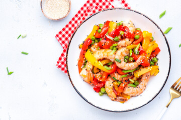 Stir fry shrimps, red paprika, green peas, chives and sesame seeds in ceramic bowl. Asian cuisine dish. White table background, top view