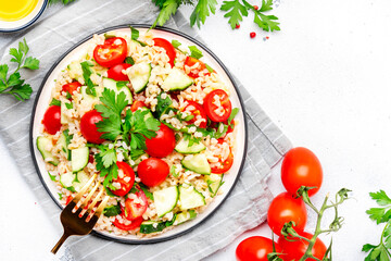 Bulgur tabbouleh salad with tomatoes, cucumbers and parsley. Traditional Middle Eastern dish. White table background, top view