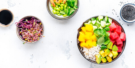 Poke bowl with raw tuna, avocado, sweet mango, cucumber, lettuce and white rice, soy sauce and sesame seeds. White table background, top view