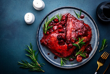 Baked duck legs in wine and cherry sauce with rosemary. Gourmet dinner with red wine gllass. Blue stone table background, top view