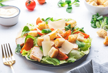 Classic Caesar salad with chicken, iceberg salad, croutons, parmesan cheese and caesar dressing. Black table background, top view