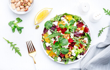 Beetroot and white cheese salad with arugula, lettuce,  orange and pistachios on white table. Fresh useful dish for healthy eating