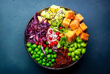 Fototapeta na wymiar Vegan buddha bowl with red quinoa, fried tofu, avocado, edamame beans, green peas, radish, cabbage, pomegranate and sesame seeds with soy sauce. Healthy diet food. Blue table background, top view
