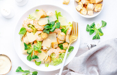 Gourmet Caesar salad with shrimp, iceberg and lettuce, croutons, parmesan cheese and caesar dressing. White table background, top view