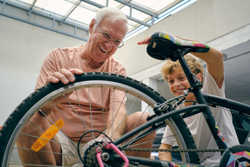 Cheerful grandfather repairing grandson bicycle in garage