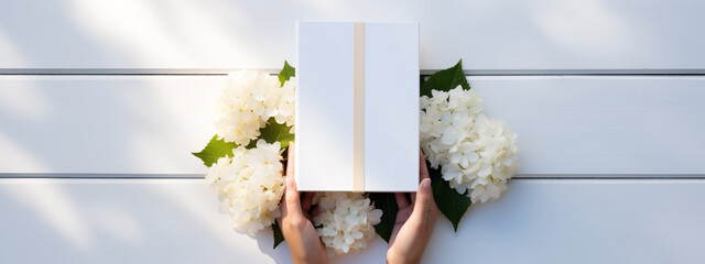 hands holding a gift, a box, on a white wooden background with hydrangea flowers. Bright sunny photography for mockups, presentations and publications.