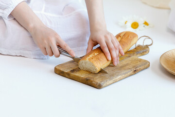 Girl cuts a loaf of bread with a knife on a wooden baking sheet on floor. Part of body