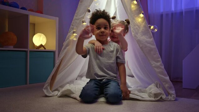 Kids friends enjoy playing in white tent together during sleepover in apartment.