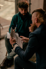 A close up shot of long hair bearded businessman reading a financial report while his male colleague is talking to him