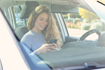 Cheerful female driver browsing smartphone in car