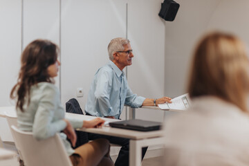 Senior male business leader listening to lecture for better efficiency at the classroom with his employees, learning new things by experienced business trainer