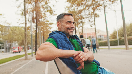 Mature man wearing casual clothes in wireless earphone enjoying music while sitting on park bench, bottom view, soft focus