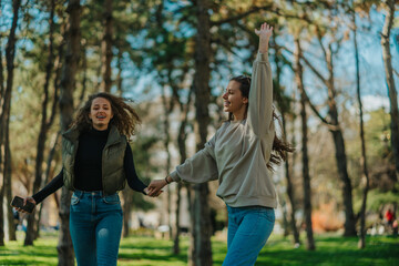 Two happy lovely girls having fun in the park. They are holding their hands and jumping while walking