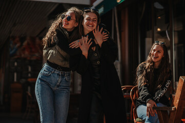 Fototapeta premium Two girls having beautiful conversation and hugging. Their female brunette friend is looking at them and smiling
