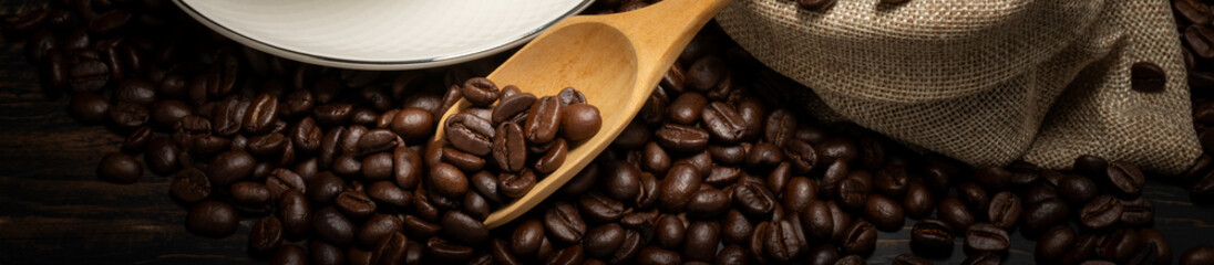 It has roasted coffee beans with a stack of wooden spoons on wooden table. Dark background.