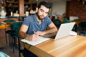 Attractive man writing while doing remote freelance work