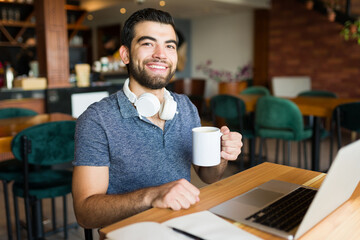 Fototapeta na wymiar Cheerful freelancer man smiling doing remote work at the cafe