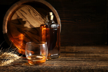 Oak barrel with bottle and glass of cold whiskey on wooden background