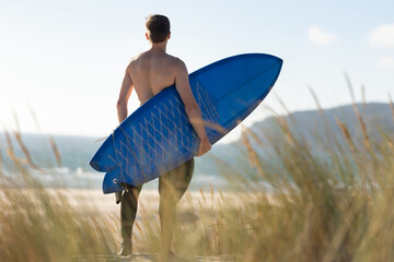 A man standing on the beach holding a blue surfboard - view from the back