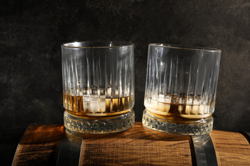 Glasses of cold whiskey on wooden barrel against dark background