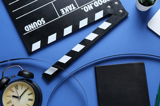 Notebook with movie clapper, film reel and alarm clock on blue background