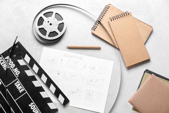 Movie clapper with storyboard, notebooks and film reel on light background