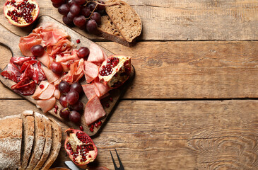 Board with assortment of tasty deli meats and bread on wooden background