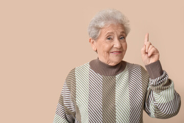 Senior woman pointing at something on beige background